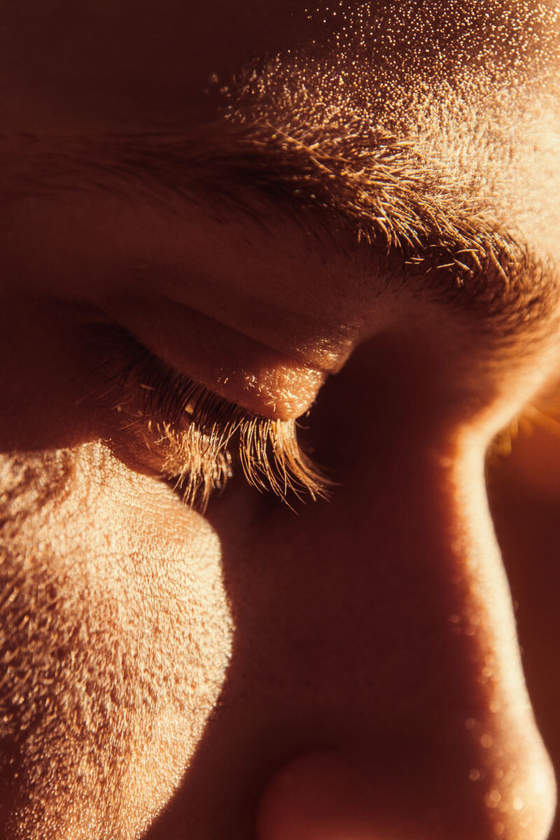An extreme close-up of a person's closed eye bathed in warm amber light, conveying quiet introspection or emotional weight.